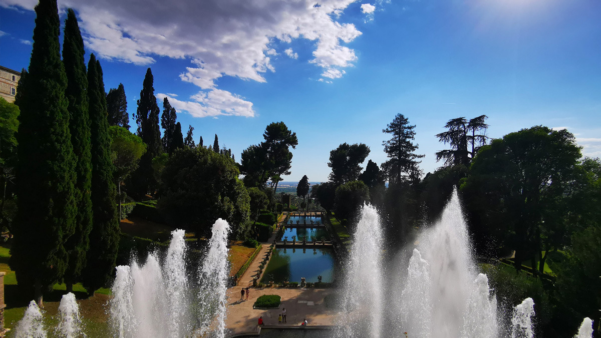 Tall water jets framing a garden view of ponds and cypress trees from above