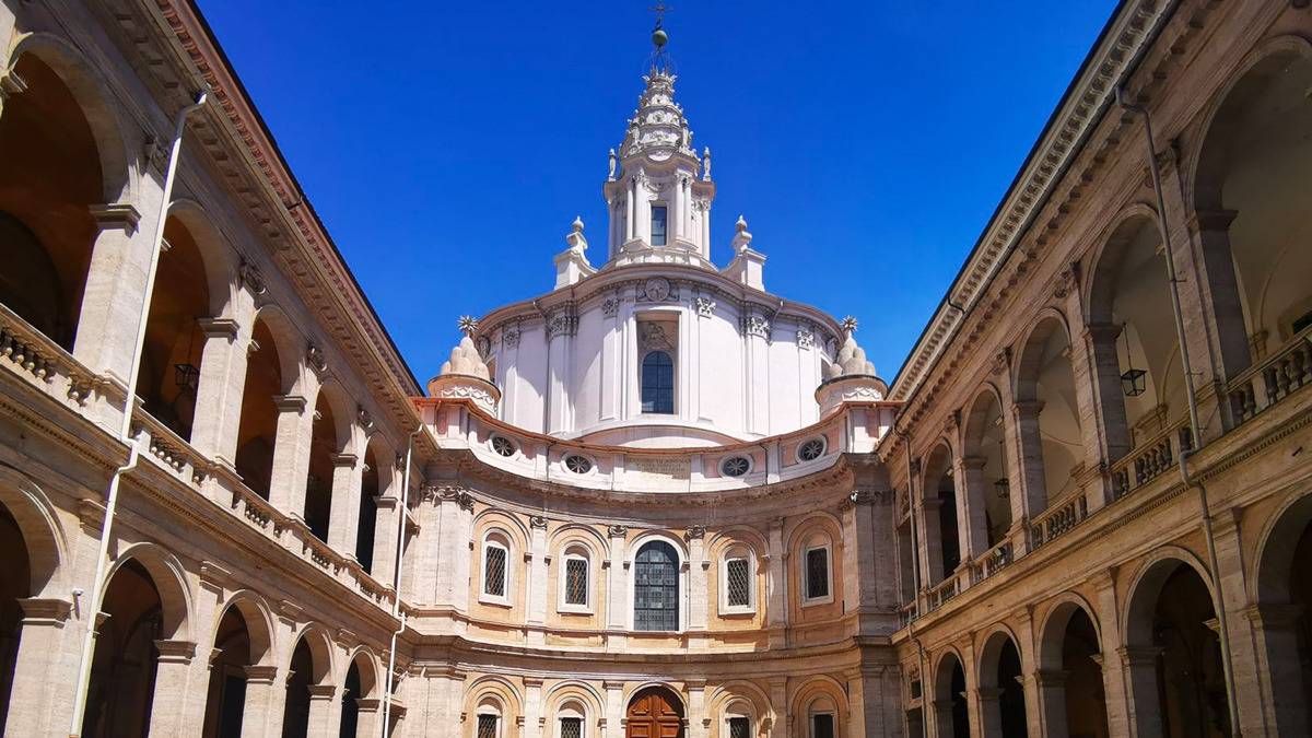Courtyard of Sant'Ivo alla Sapienza with its curved facade and spiral lantern against a blue sky