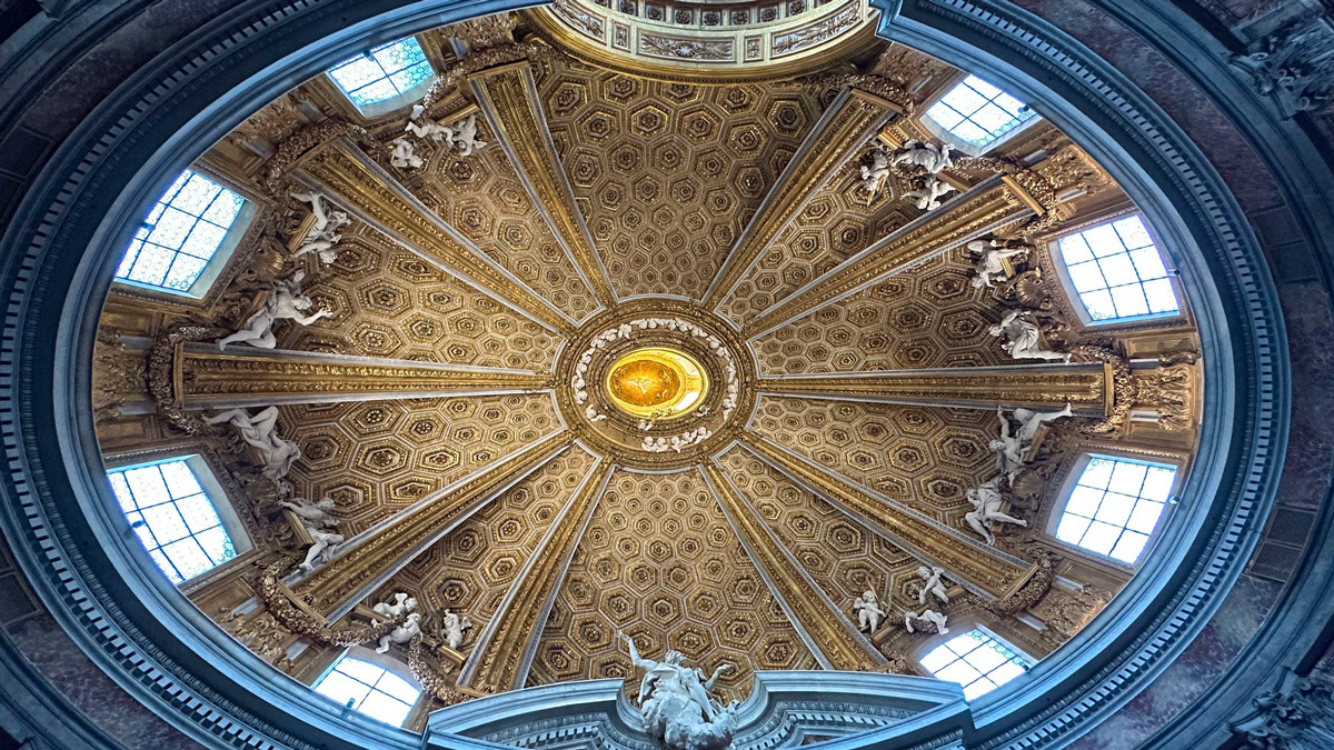 Oval gilded dome with coffers, stucco figures and windows seen from below in a Baroque church