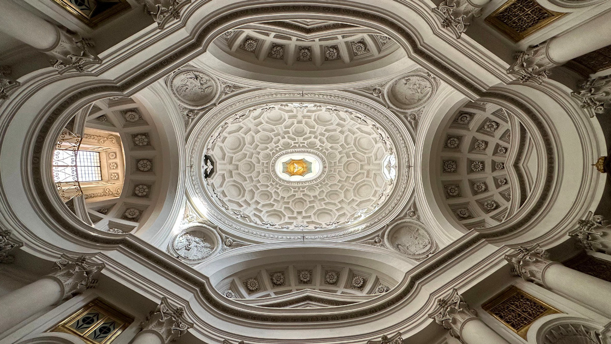Ornate white oval dome with a honeycomb of coffers in a small Baroque church ceiling