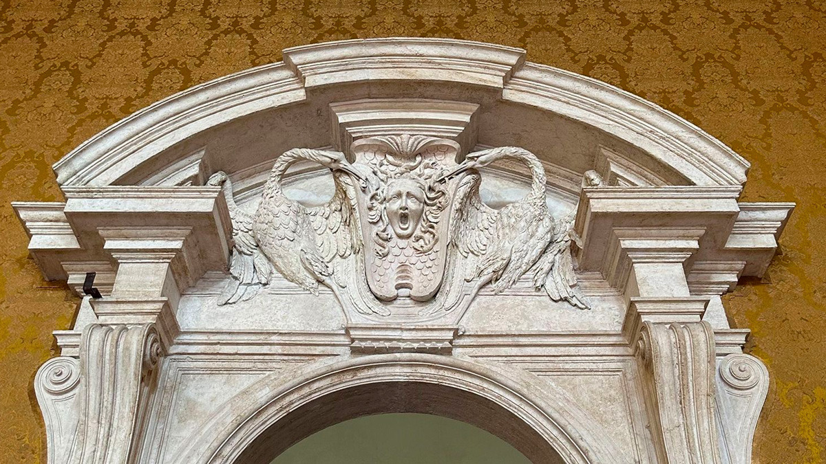 Stone doorway pediment with two swans and a carved face against golden damask walls