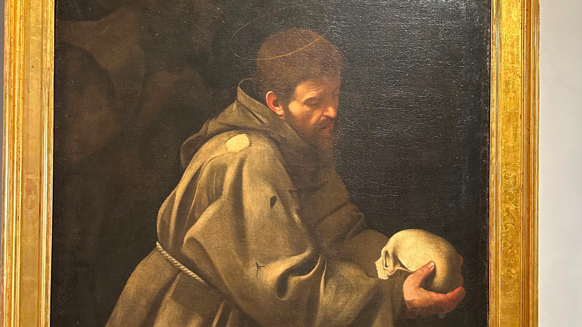 Painting of a hooded monk with a halo contemplating a skull in a gilded frame