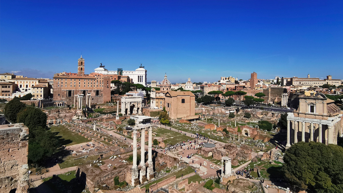 Aerial view over the ruins and columns of the Roman Forum under a clear blue sky