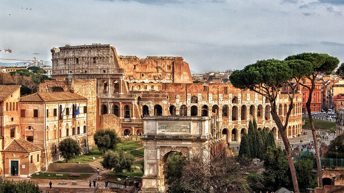 The Colosseum and a triumphal arch seen over Roman rooftops and umbrella pines