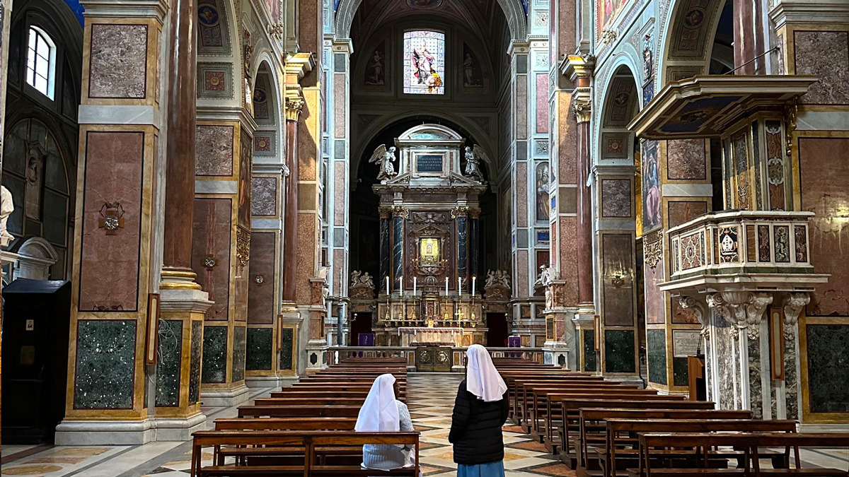 Rome church interior with a gilded altar and two nuns praying in the pews