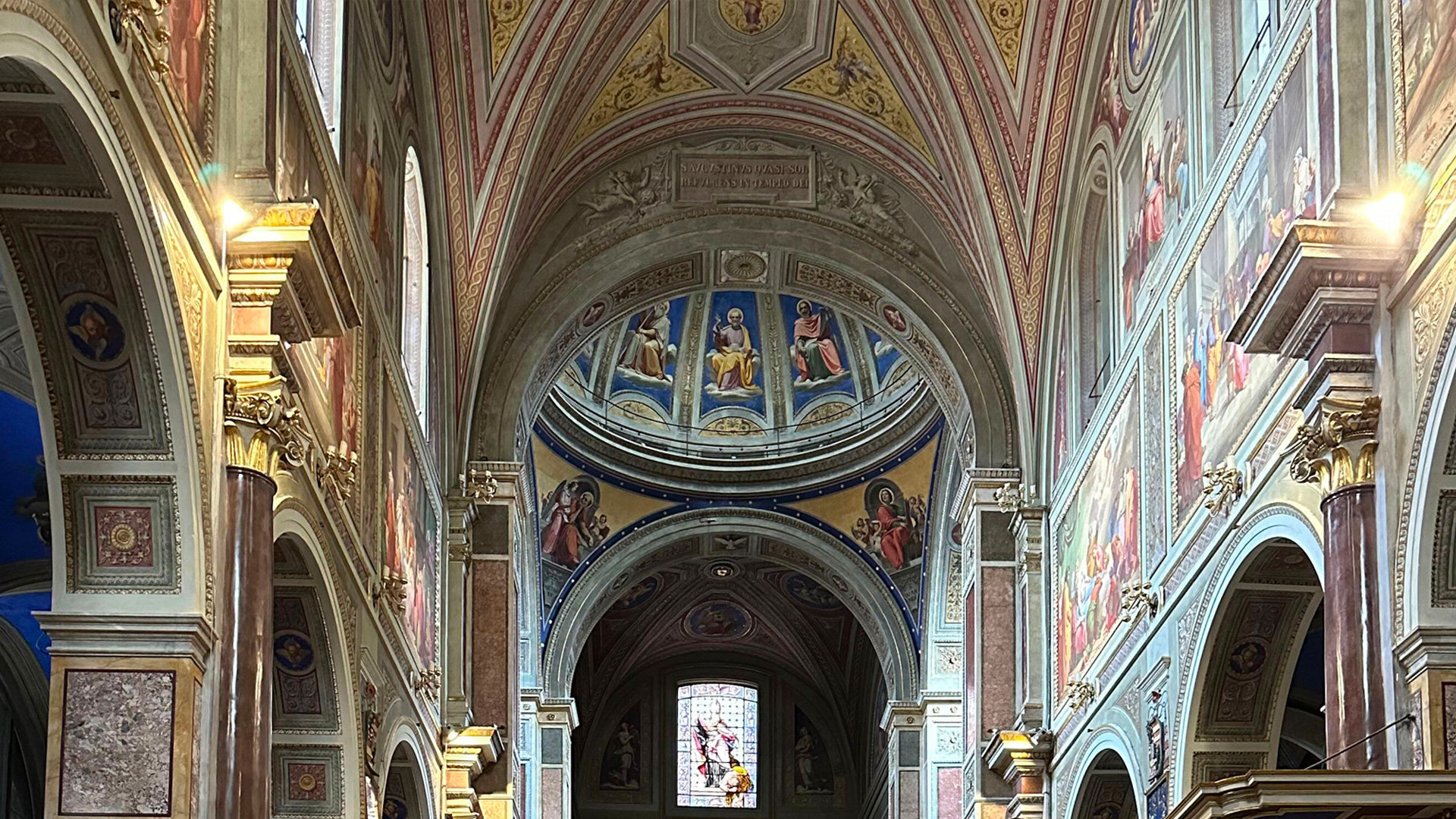 Frescoed nave and apse of a Roman church with painted arches and a stained-glass window