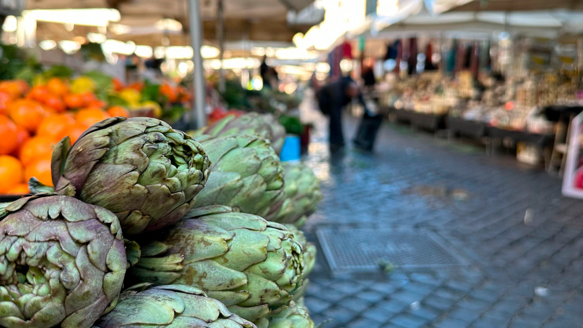 Pile of green artichokes in the foreground of an open-air Roman market
