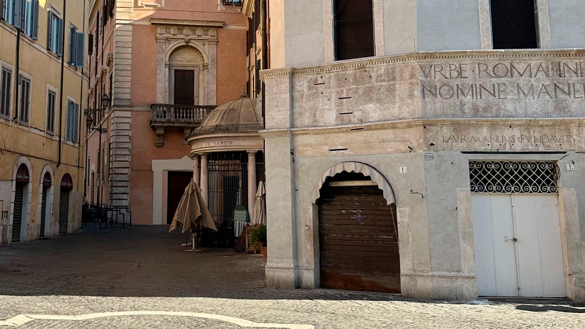 Quiet Roman square with a pink palazzo and a stone wall bearing a Latin inscription
