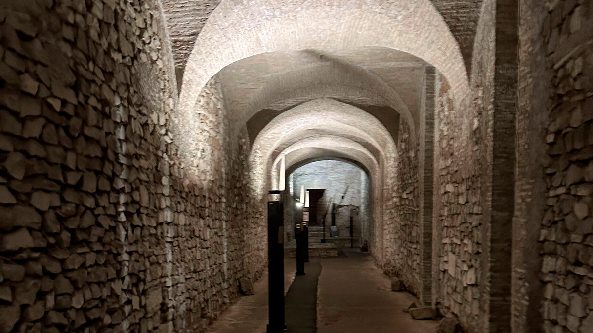 Narrow underground passage with rough stone walls and layered brick arches receding into the distance