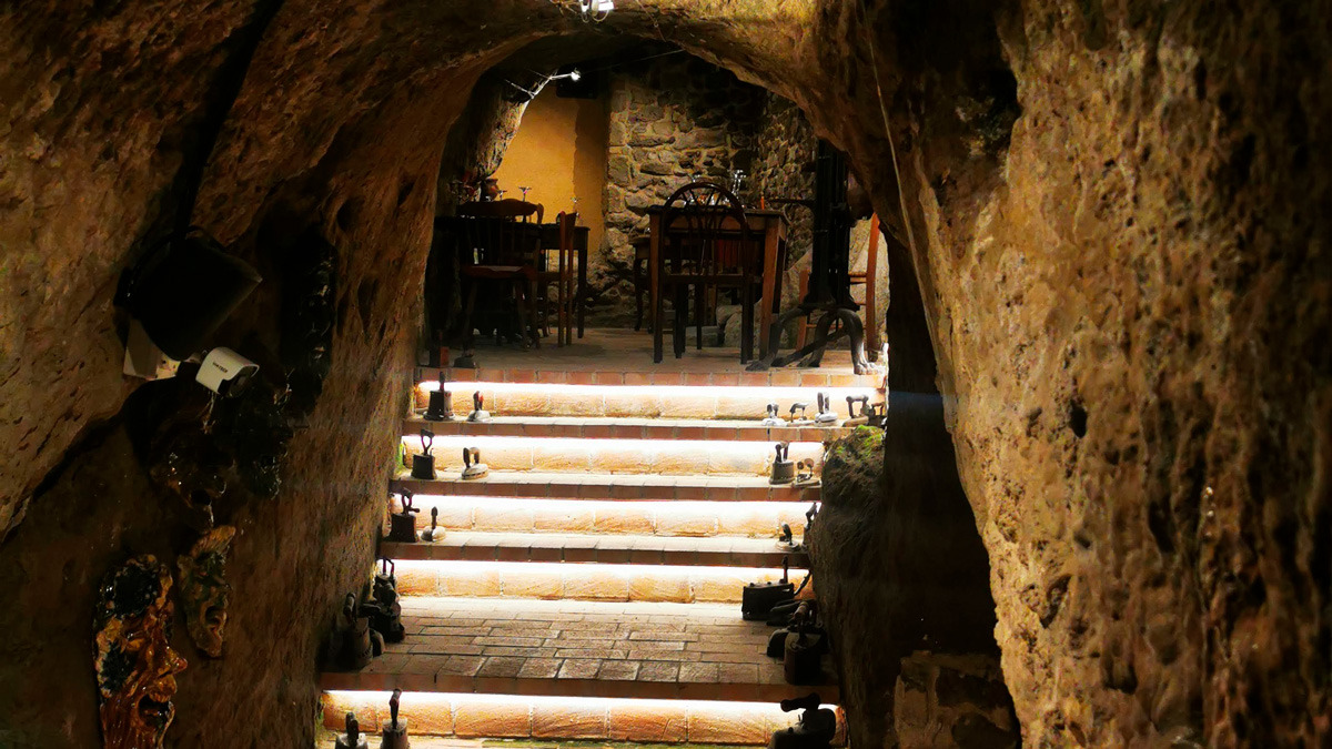 Rustic stone-vaulted cellar with lit steps leading down to a rock-walled dining room
