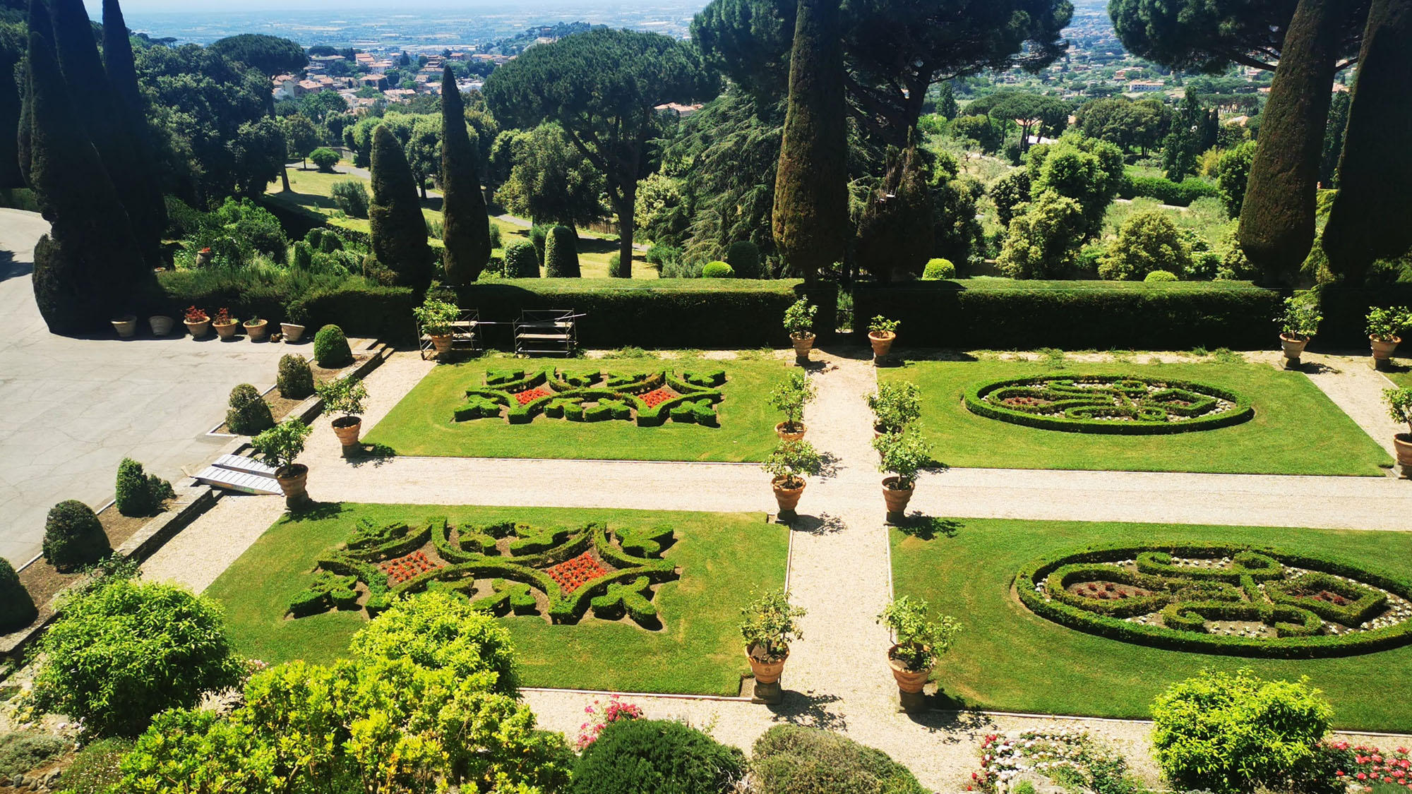 Terraced garden with embroidered flowerbeds and pots seen from above, hills in the distance