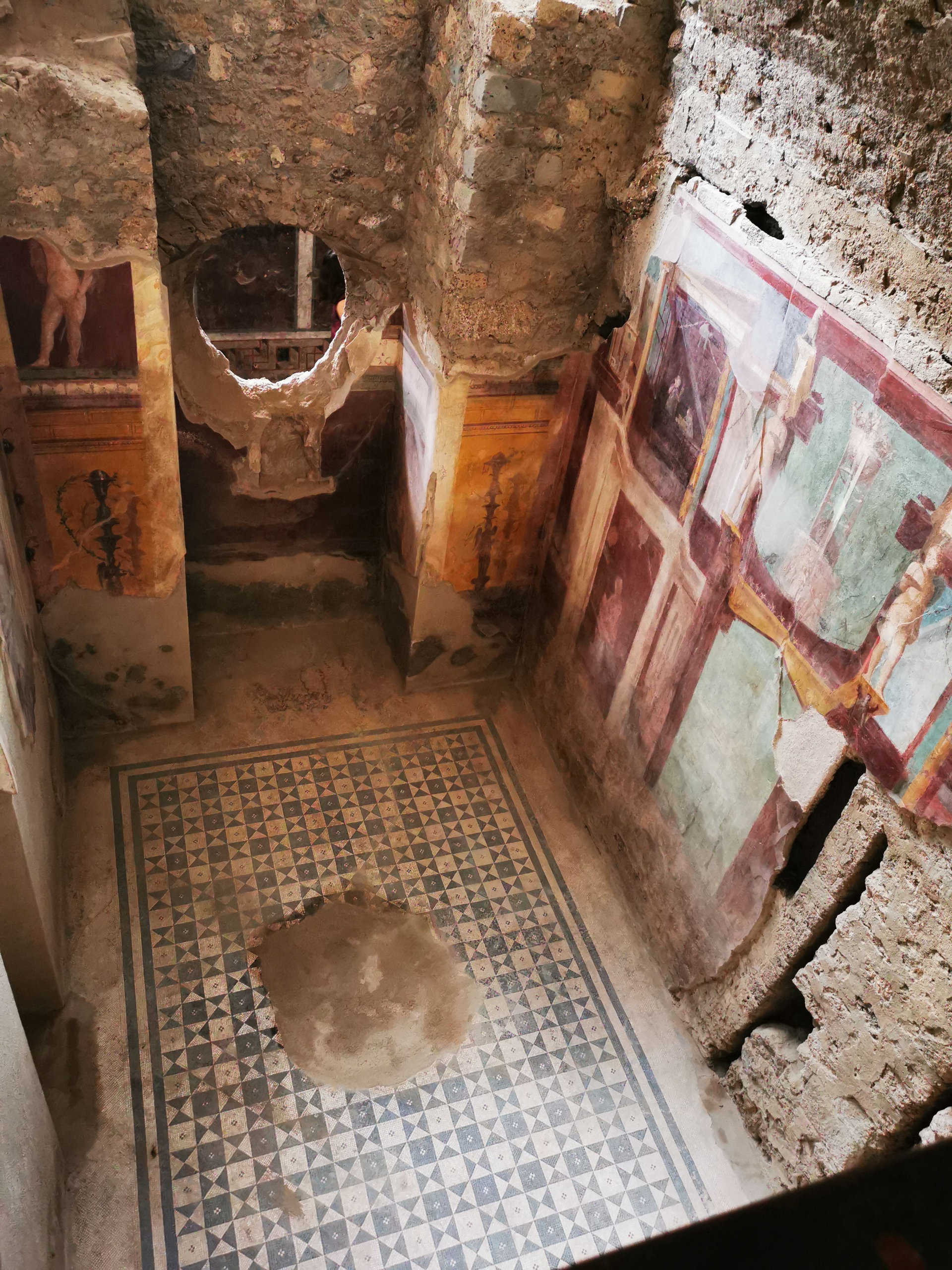 Ancient Roman room with a geometric mosaic floor and painted wall frescoes seen from above