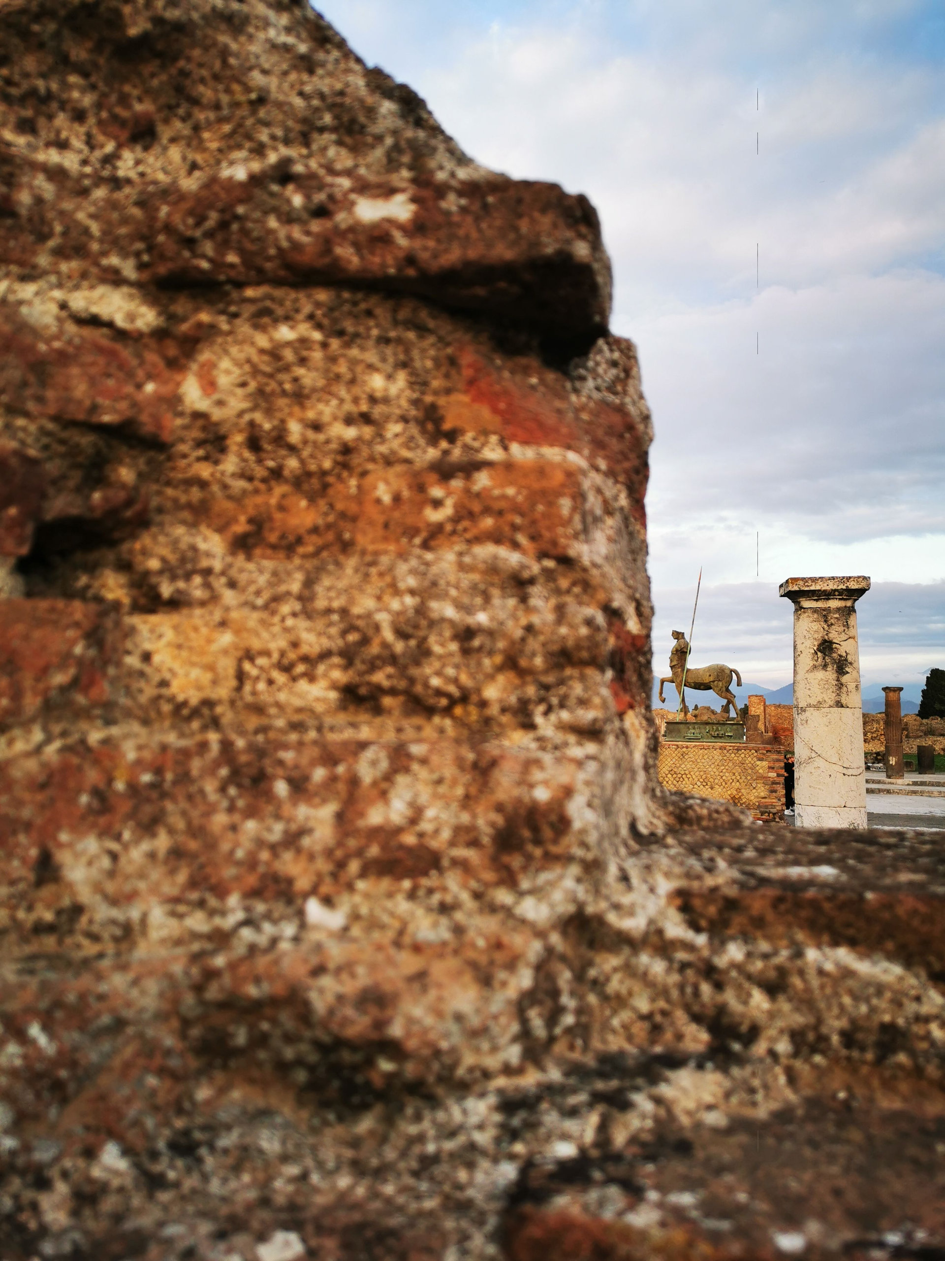 Weathered red and ochre masonry in close-up with a column and a statue blurred in the distance