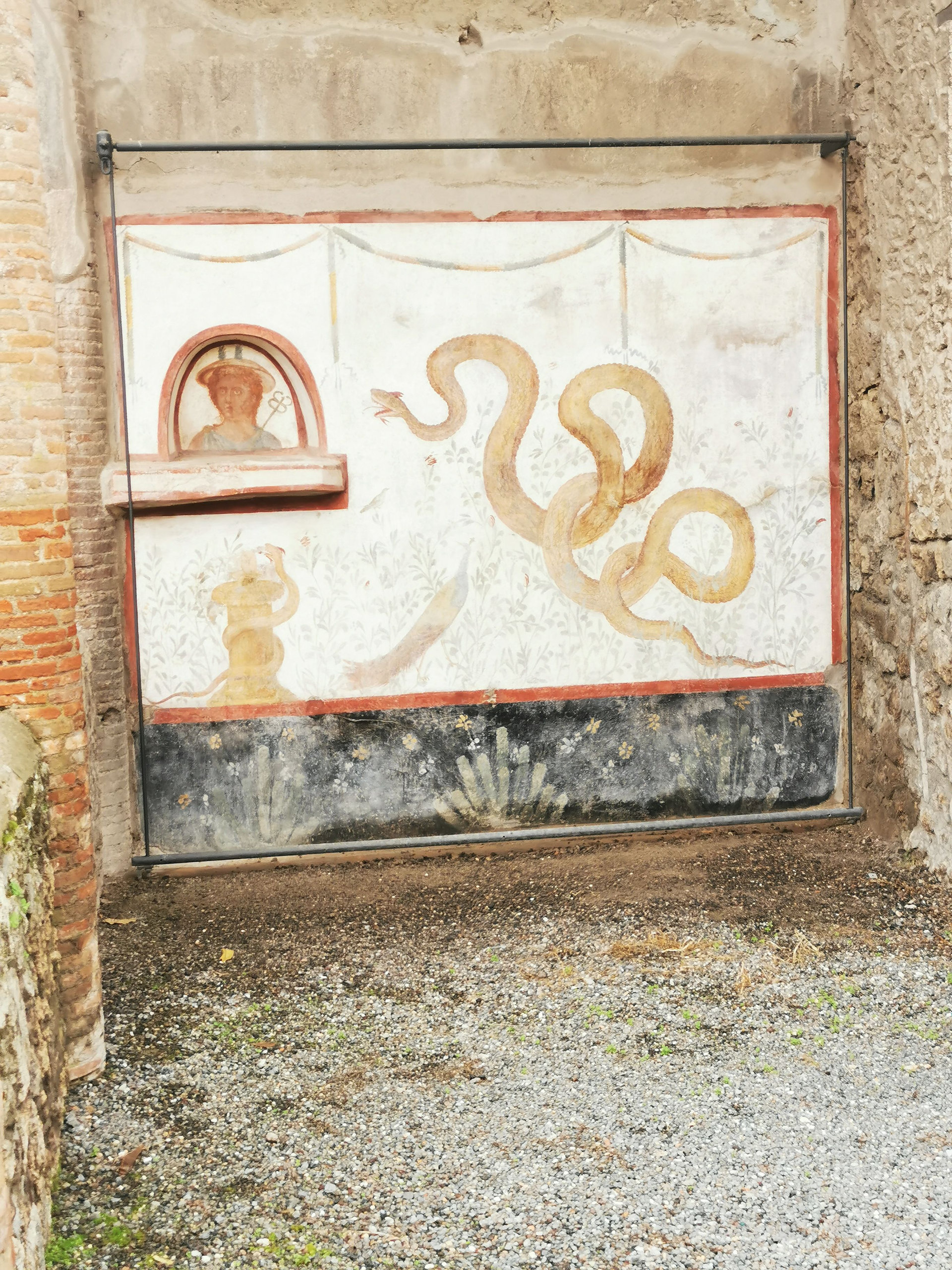 Wall fresco of a large serpent beside a small niche with a painted figure in an open-air shrine