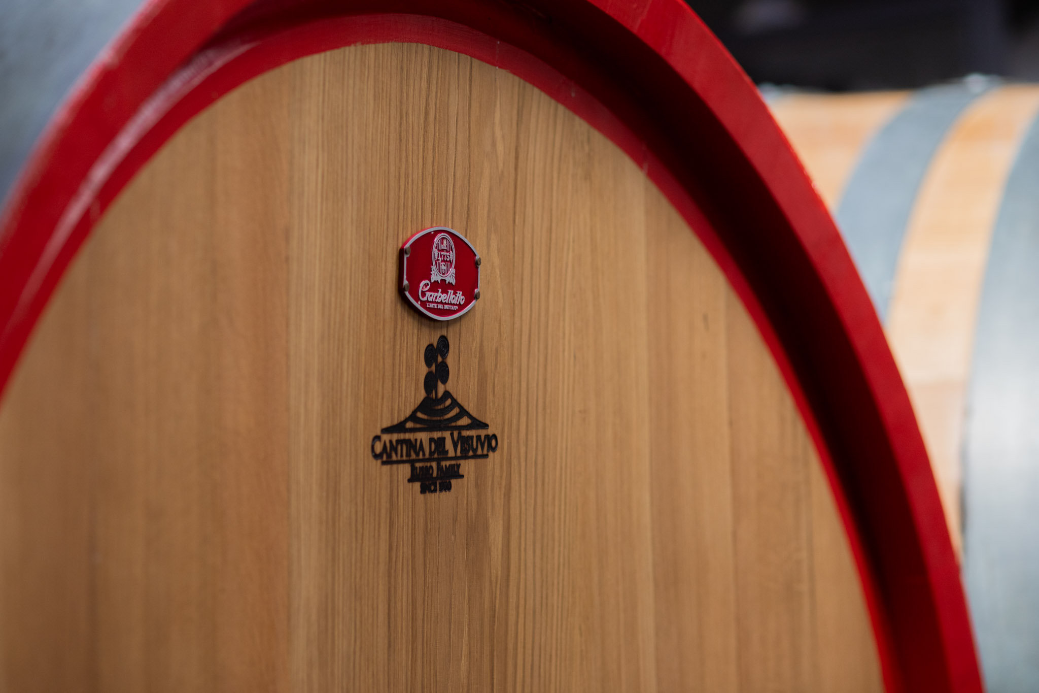 Large oak wine barrel with a red rim and a vineyard emblem