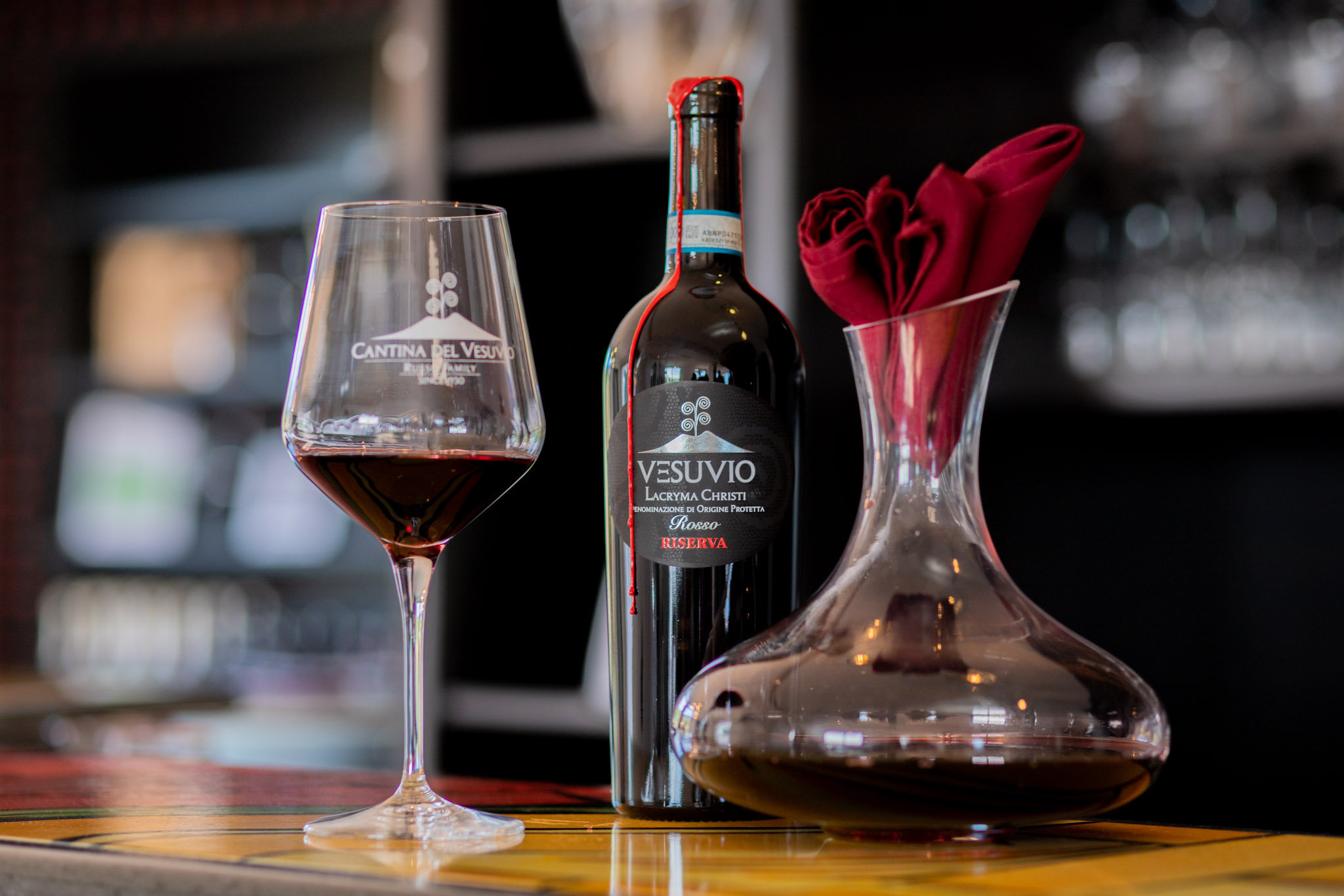 Glass of red wine, a bottle of Lacryma Christi and a decanter on a bar counter