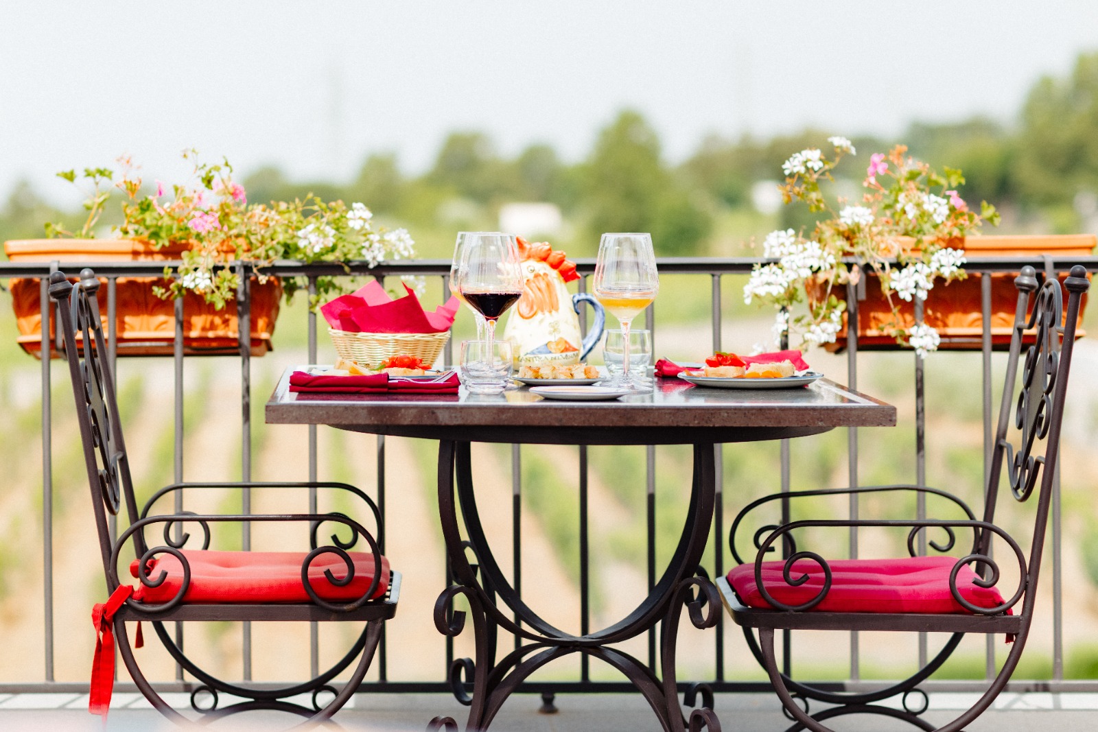 Wine and snacks laid on a small table with two iron chairs on a vineyard terrace