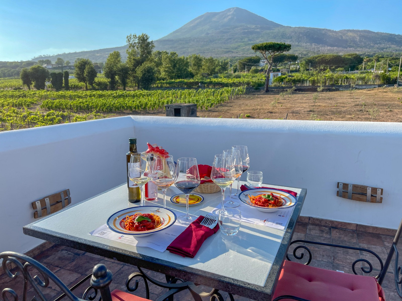 Pasta plates and wine glasses on a terrace table overlooking vineyards and Mount Vesuvius