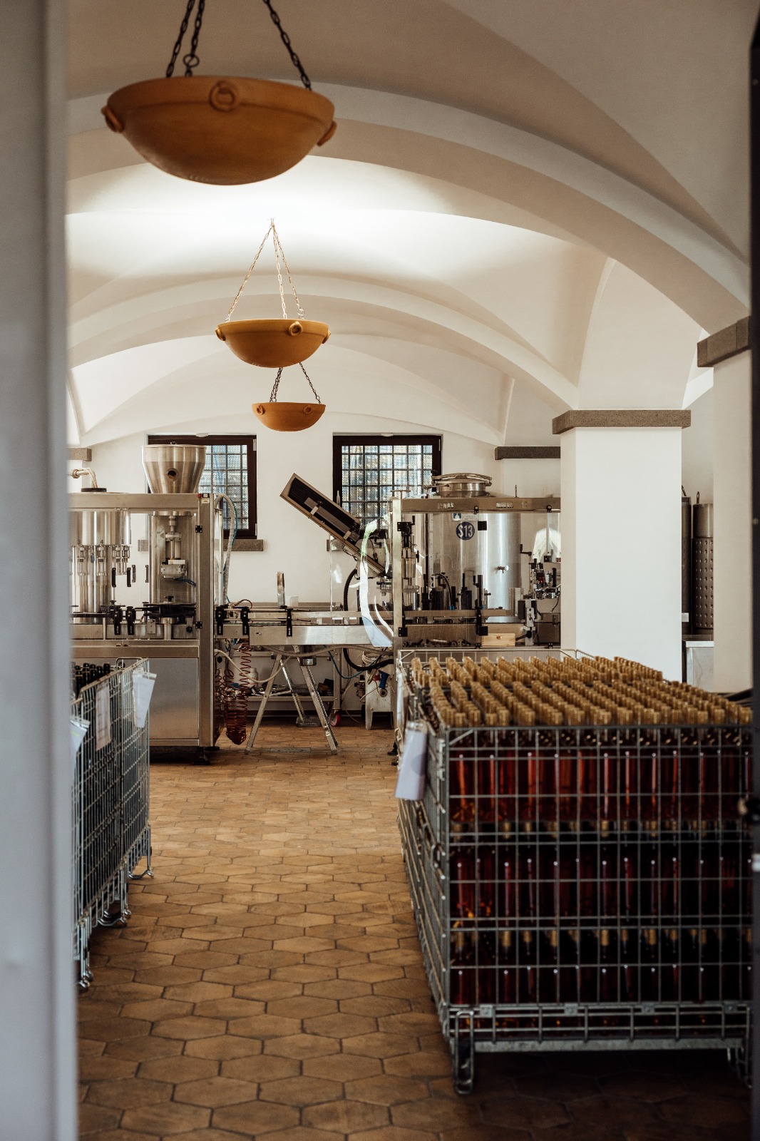 Vaulted winery cellar with steel tanks and a crate of bottles resting on a hexagonal tile floor