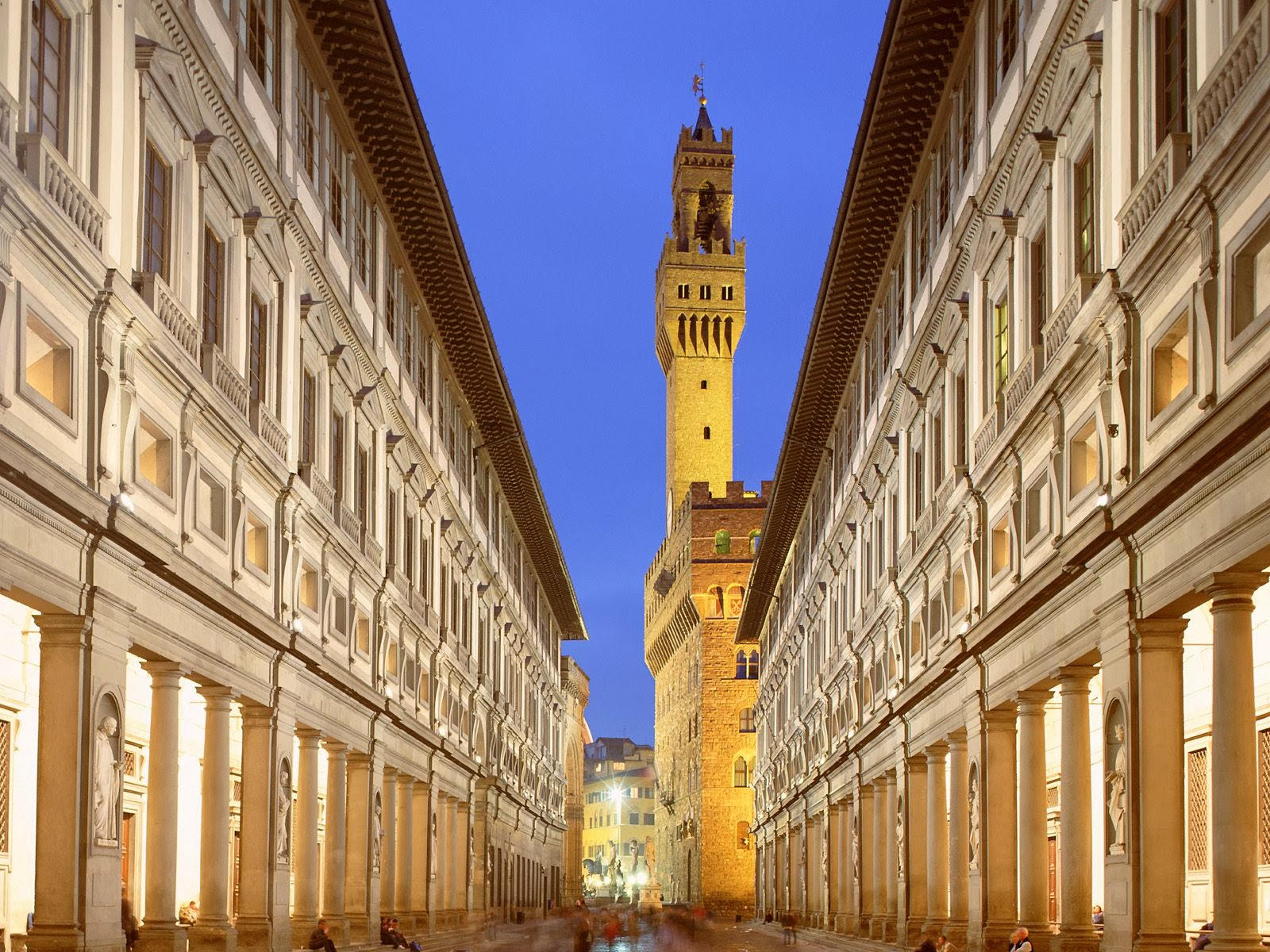 Uffizi Gallery's long arcaded courtyard glowing at dusk with the Palazzo Vecchio tower at the end