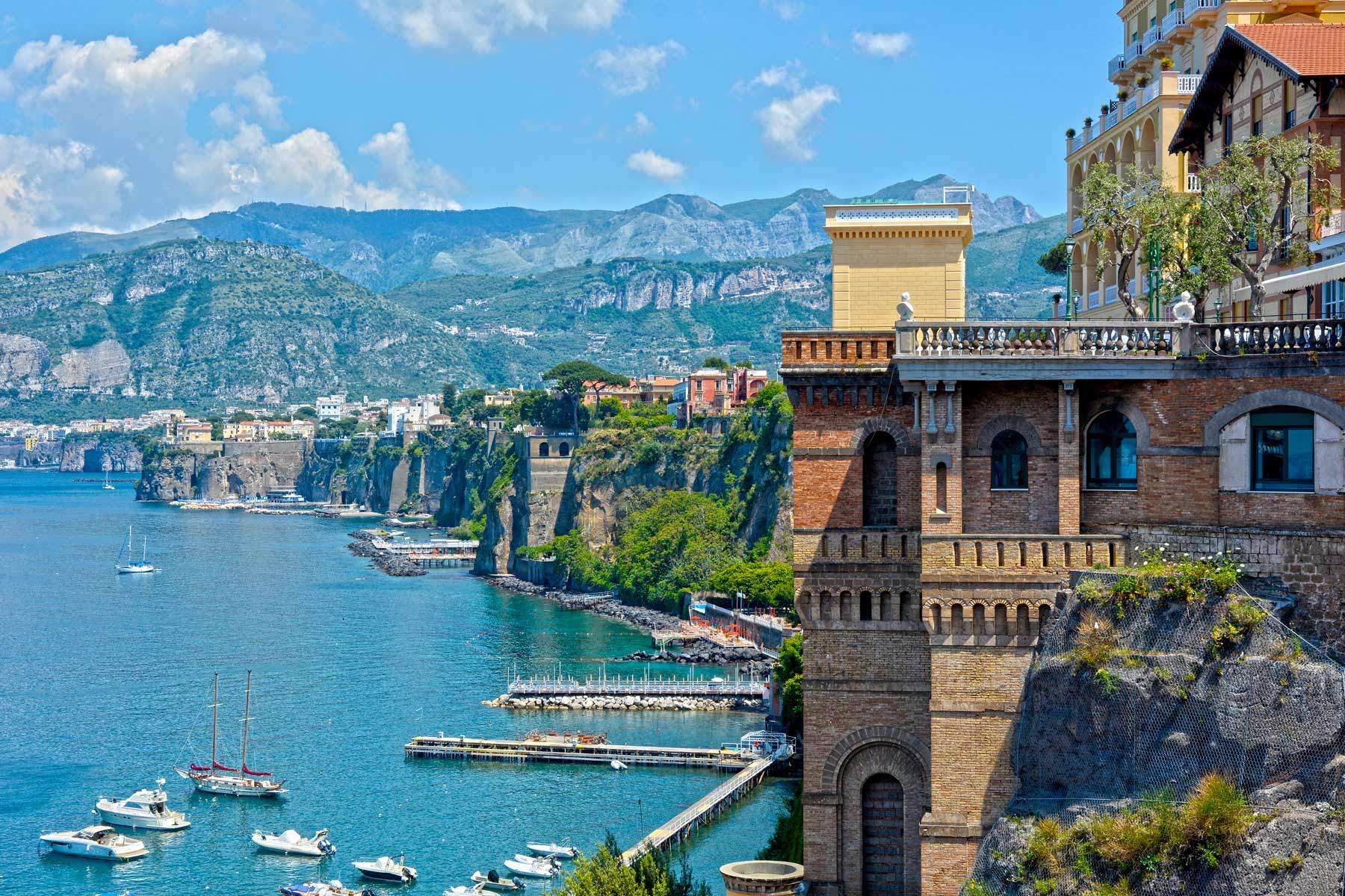 Sorrento's rocky coast with a jetty, small boats and a turreted building on the clifftop