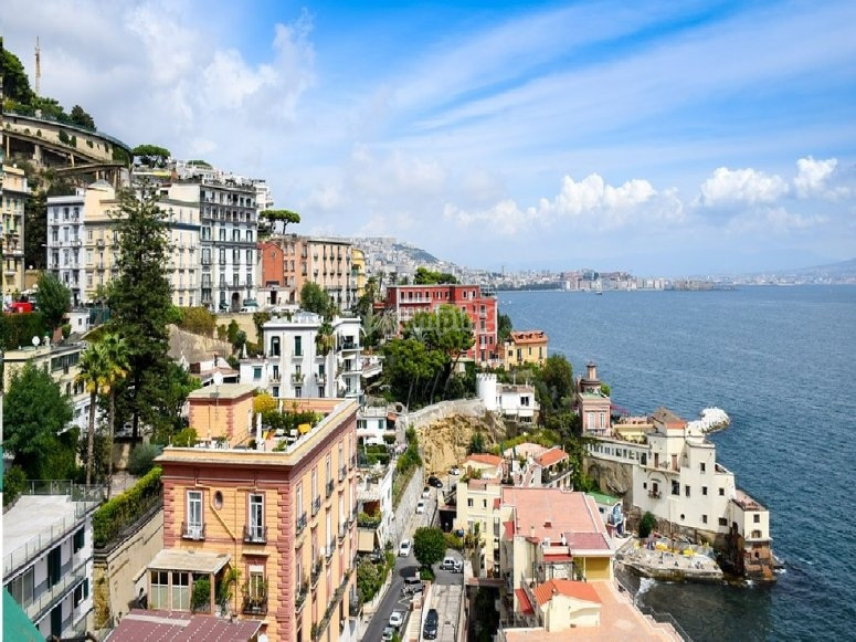 Pastel houses along the Naples coastline curving over the sea toward the city in the distance