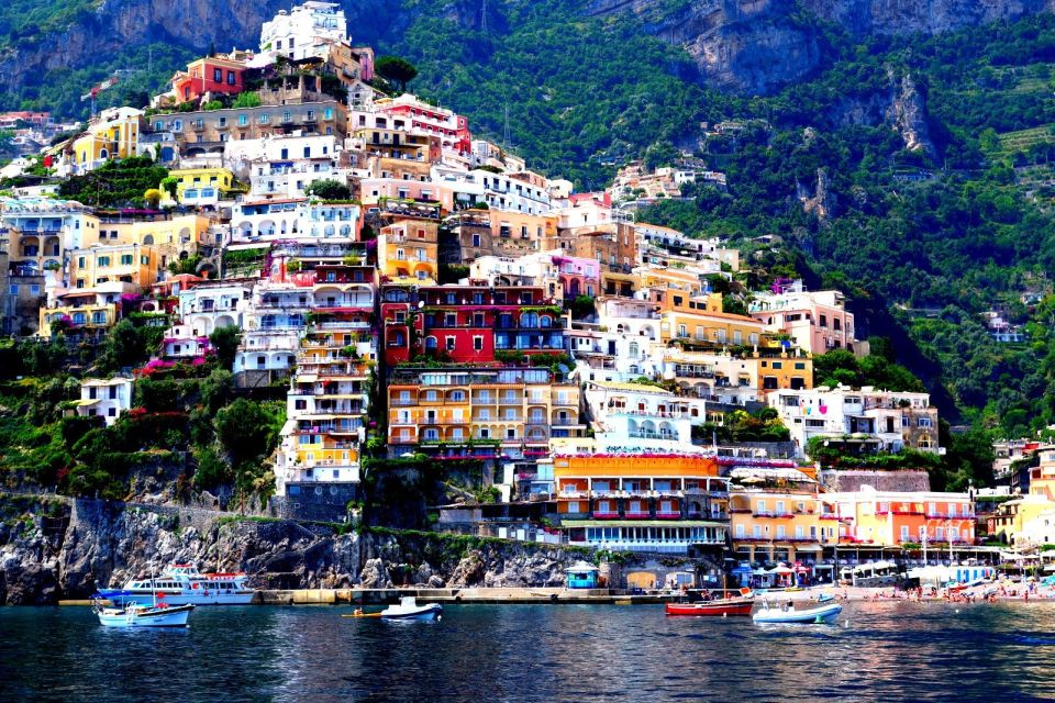 Pastel houses stacked up a steep green hillside above the sea in Positano
