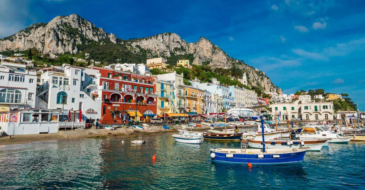Colourful waterfront houses and moored boats below limestone cliffs on a sunny day