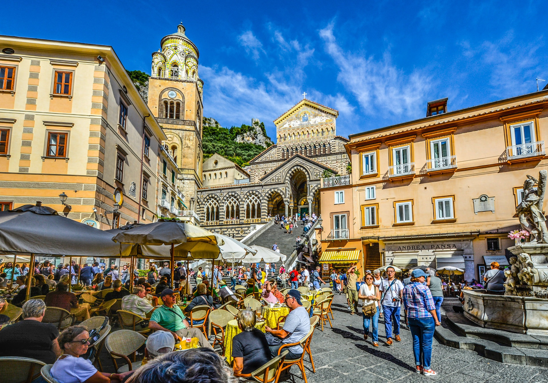 Cafe tables in a lively piazza facing Amalfi cathedral and its tall bell tower