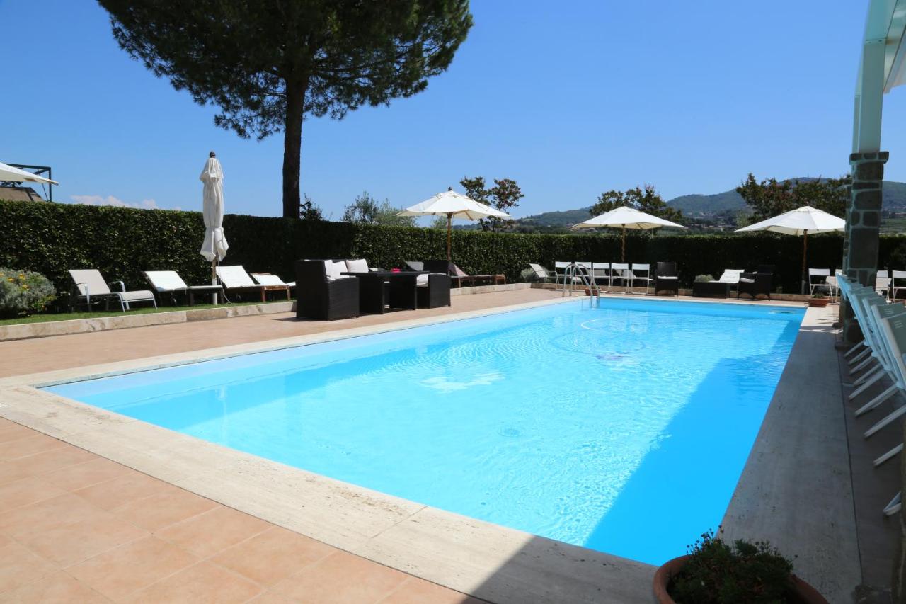 Sunlit swimming pool with loungers and parasols surrounded by a clipped hedge and hills