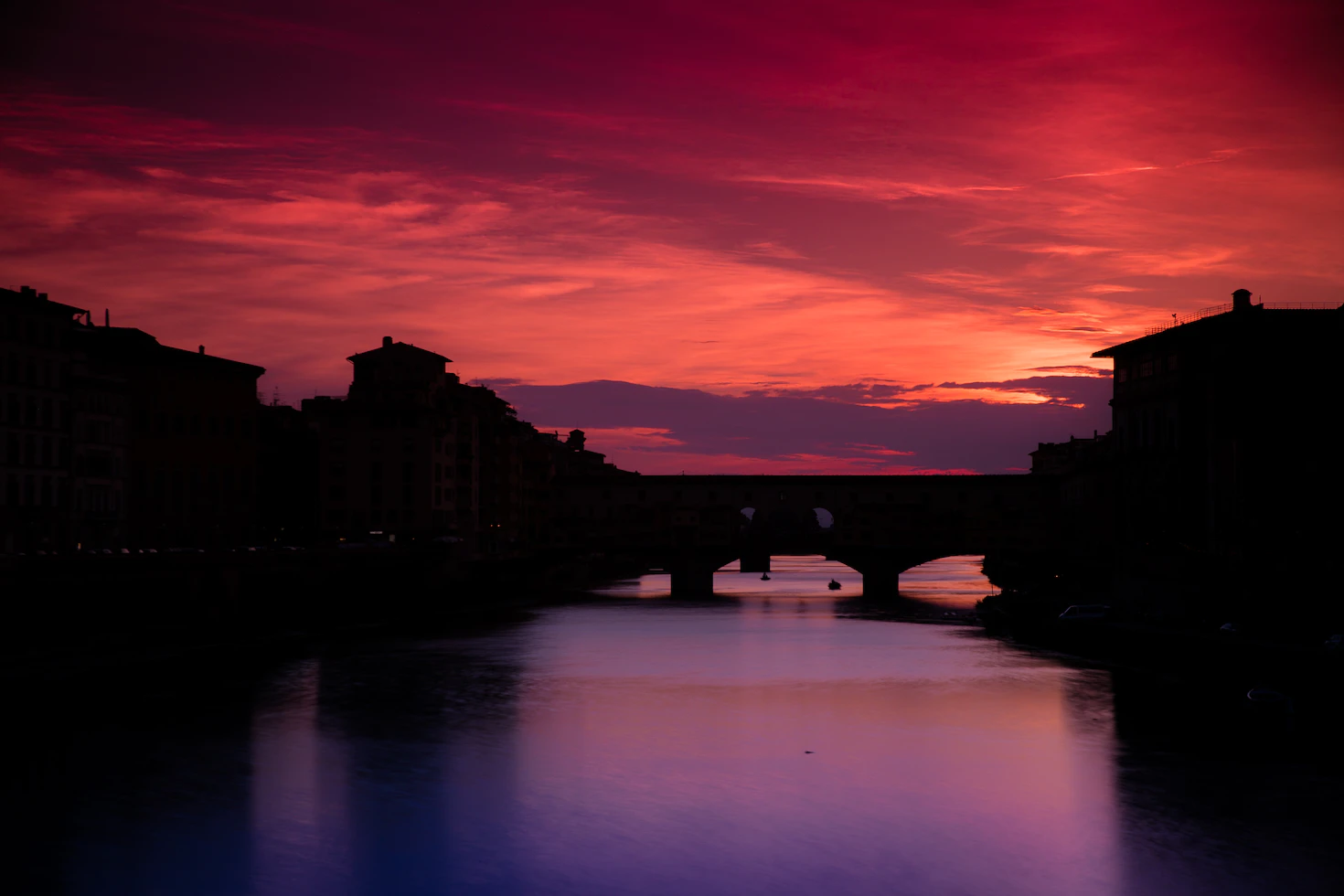 Silhouette of Ponte Vecchio under a vivid red and purple sky reflected in the river