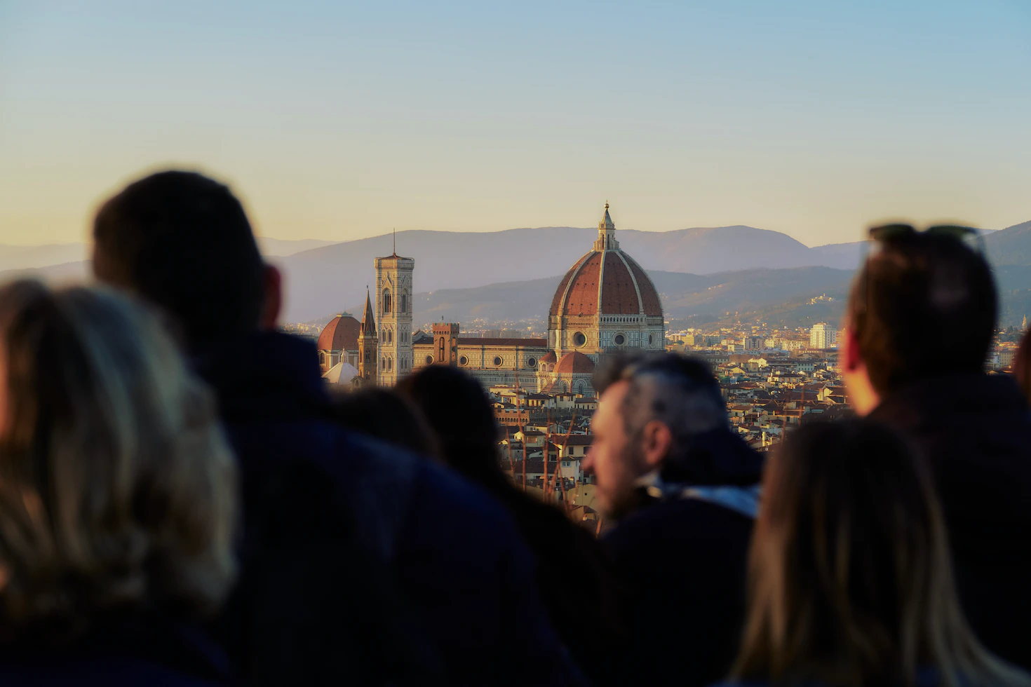 Crowd of travellers with blurred heads watching the Florence Duomo and bell tower in golden light