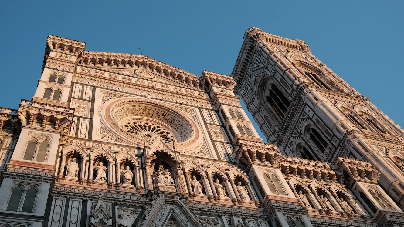 Marble facade of Florence Cathedral and Giotto's bell tower seen from below in warm sunlight