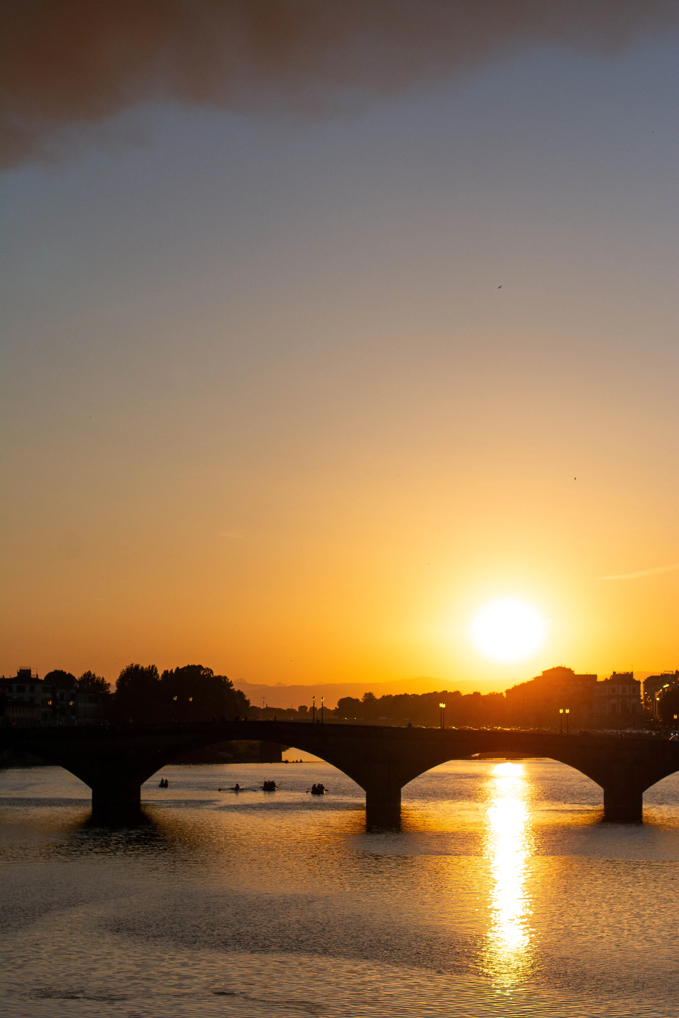Setting sun and its golden reflection on the Arno beside a stone bridge