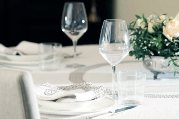 Elegant table setting with wine glasses, folded napkin and white roses in a silver vase