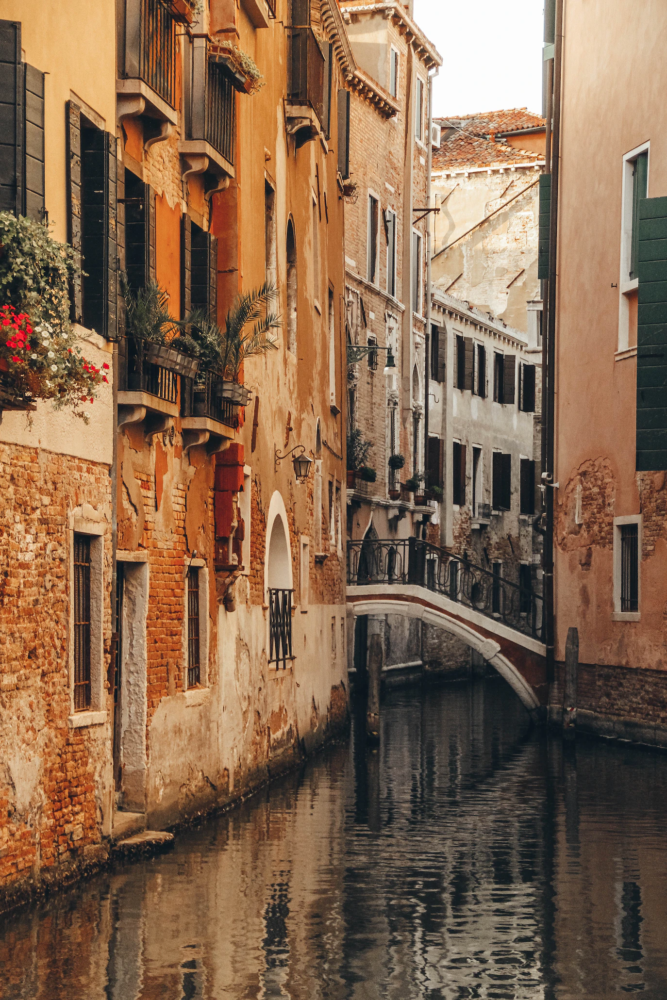 Narrow Venetian canal with terracotta-coloured houses, flower-filled balconies and a small stone bridge