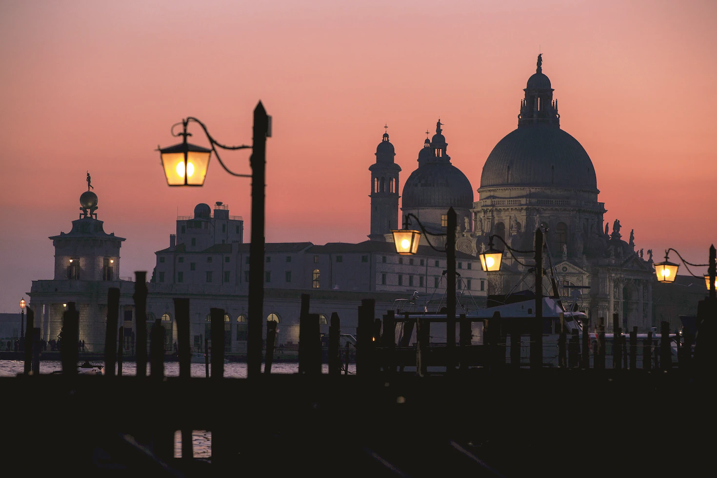 Venetian church domes and street lamps silhouetted against a pink sunset sky