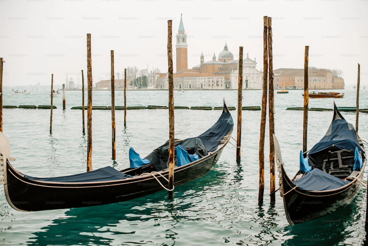 Moored gondolas covered in blue tarpaulins with San Giorgio Maggiore across the misty lagoon