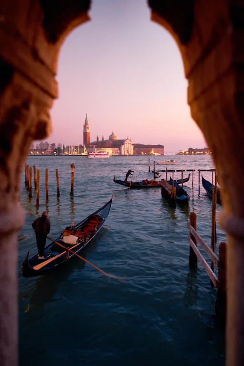 Gondola and gondolier seen through a stone archway towards San Giorgio Maggiore at dusk