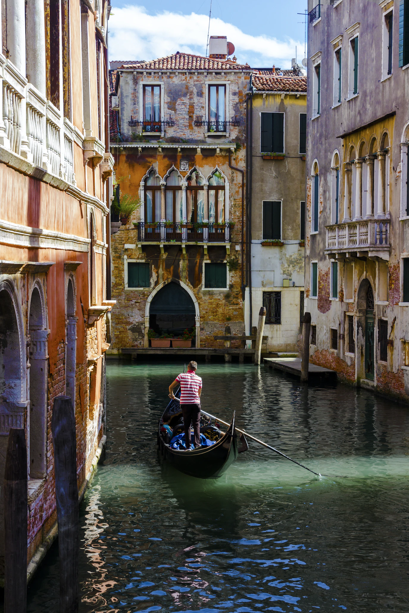 Gondolier rowing along a green canal between weathered palazzi with Gothic windows