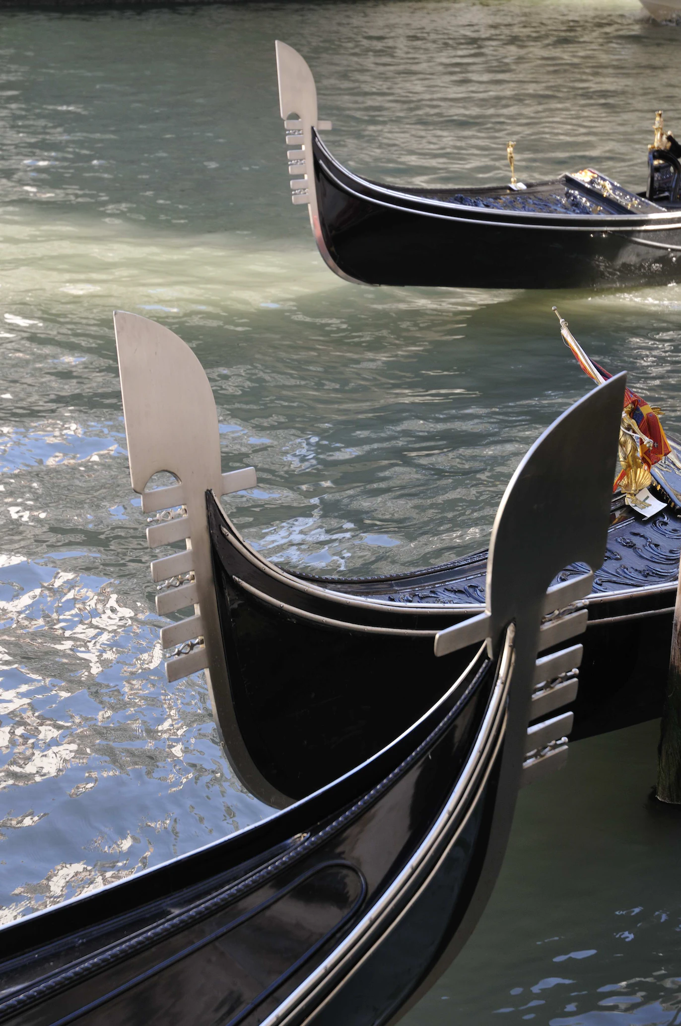 Polished steel prows of black gondolas close up, glinting over the water