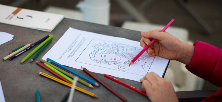 A child colouring a drawing of a woman's portrait with pencils spread across a table