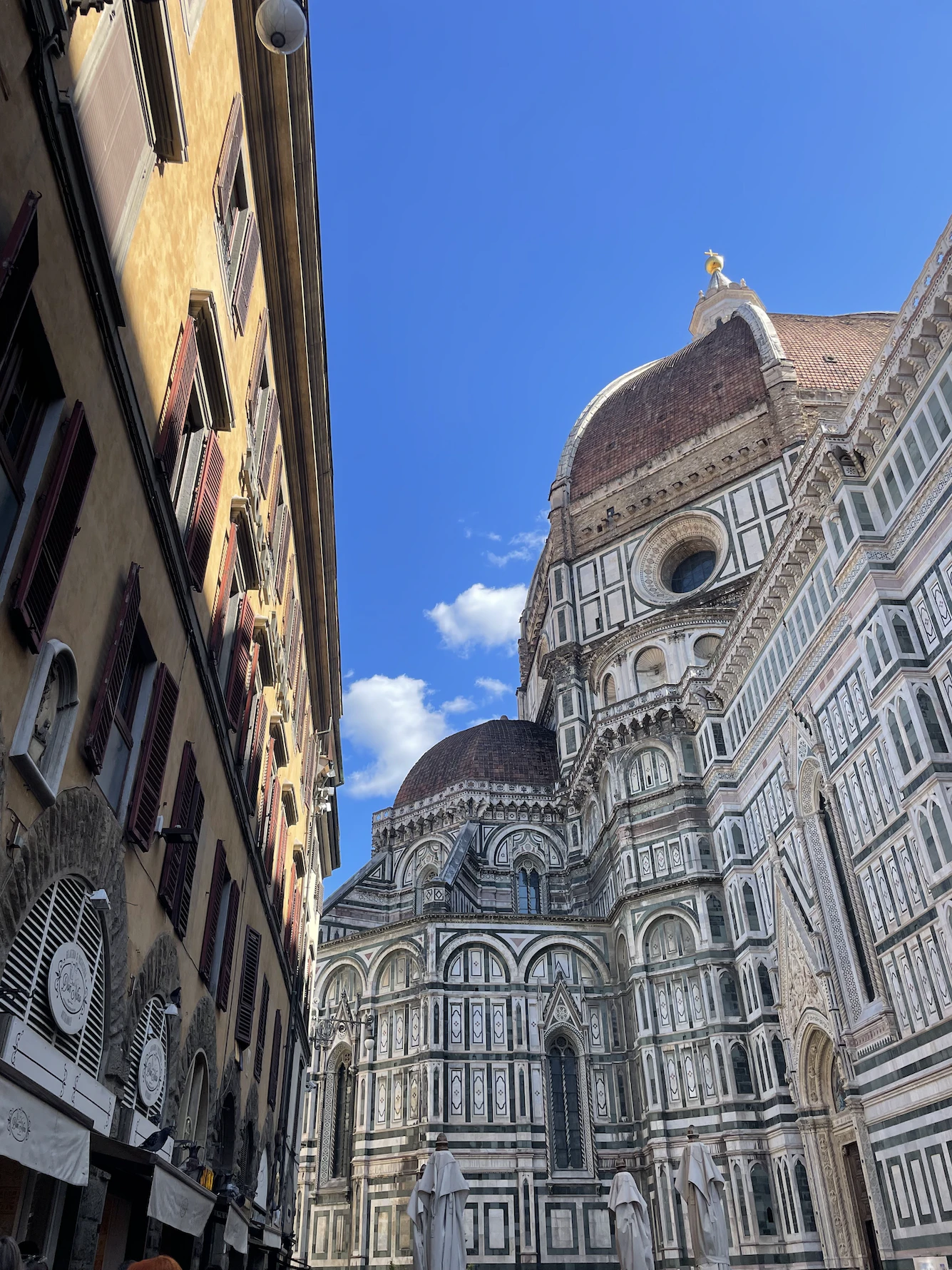 Florence Cathedral's marble facade and red dome rising above an ochre street under a blue sky