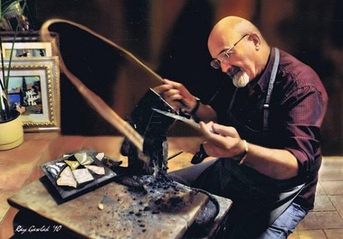 Craftsman with glasses cutting small stone pieces on a traditional bow-powered saw for a mosaic