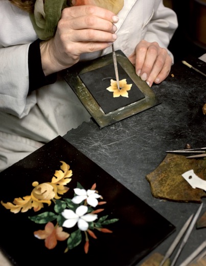 Artisan placing a flower inlay with tweezers, a finished pietra dura floral panel in the foreground