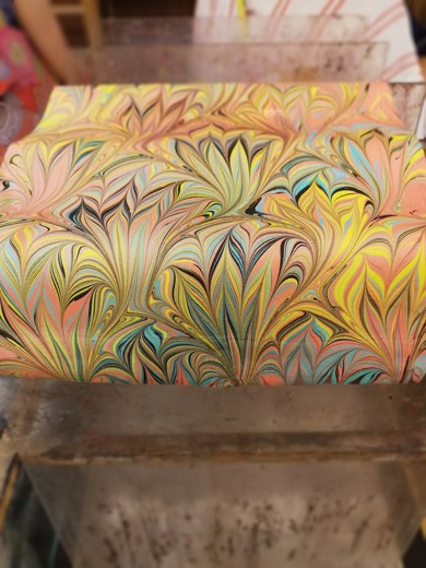 Hand-marbled paper with swirling feather patterns in pink, yellow and teal