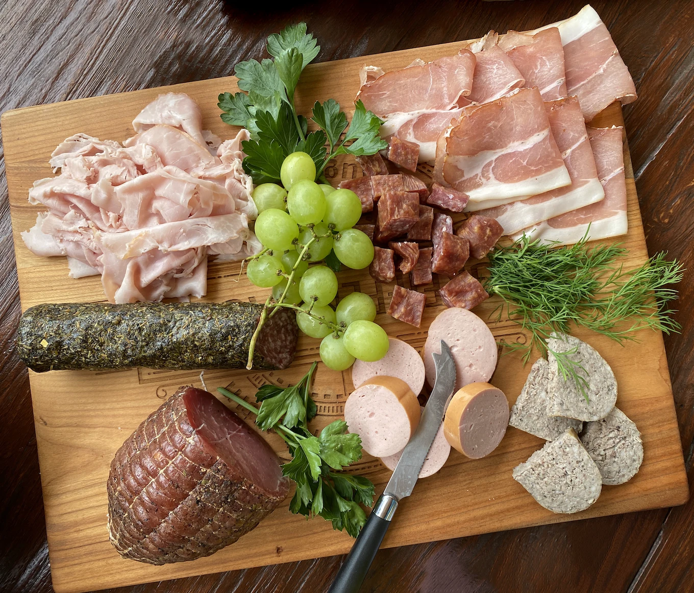 Wooden board of cured meats with prosciutto, salami, grapes and fresh herbs