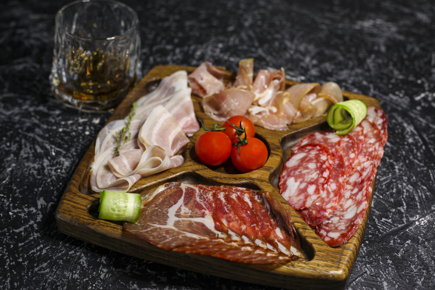 Platter of sliced cured meats and cherry tomatoes on a wooden serving tray