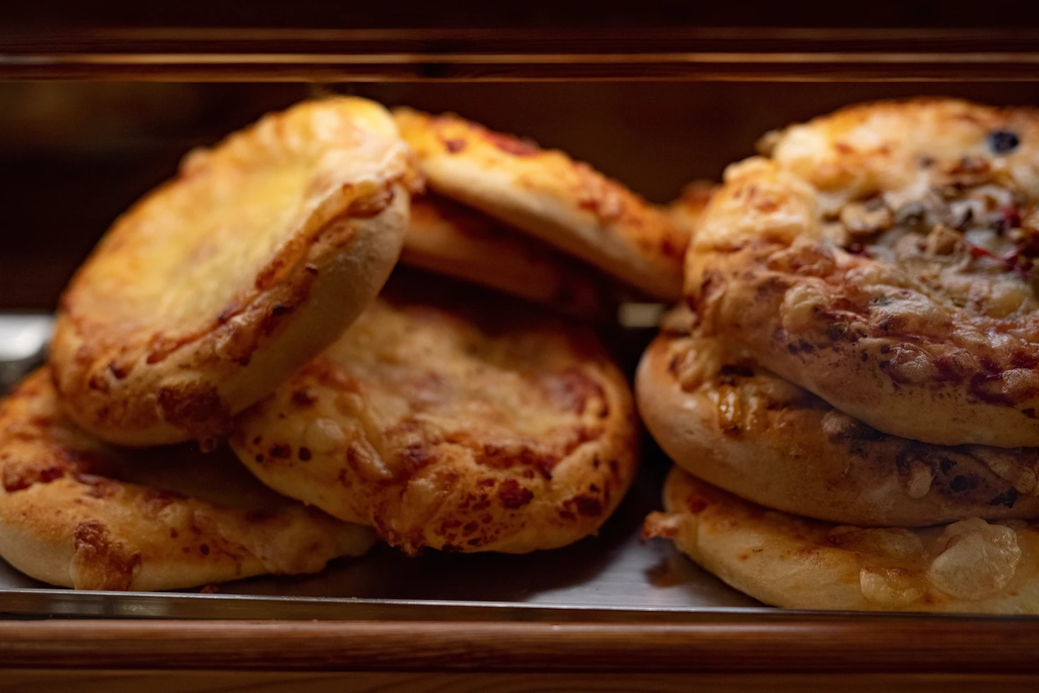 Stack of freshly baked pizzette topped with melted cheese in a bakery window