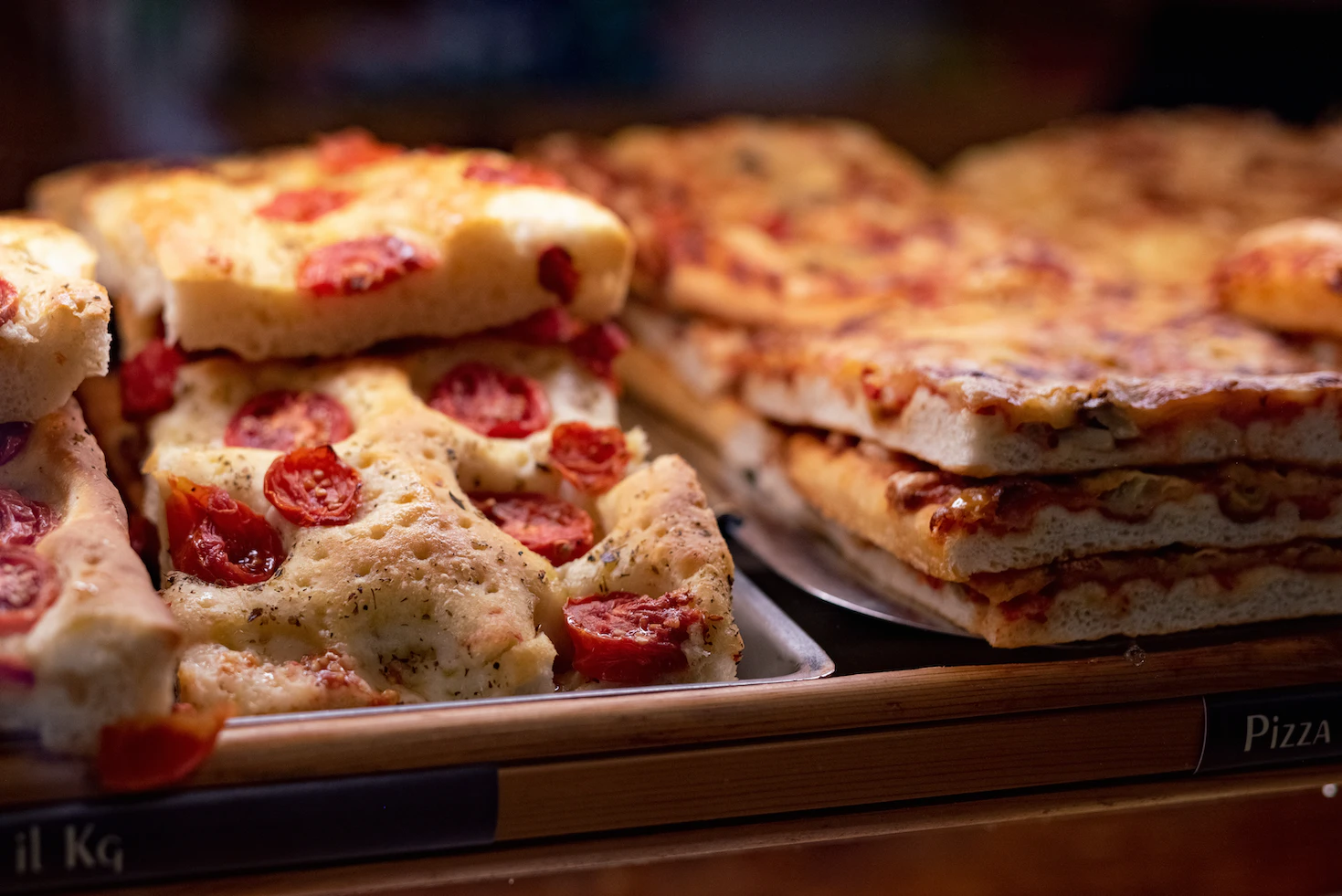 Trays of pizza al taglio and tomato focaccia displayed in a Florentine bakery